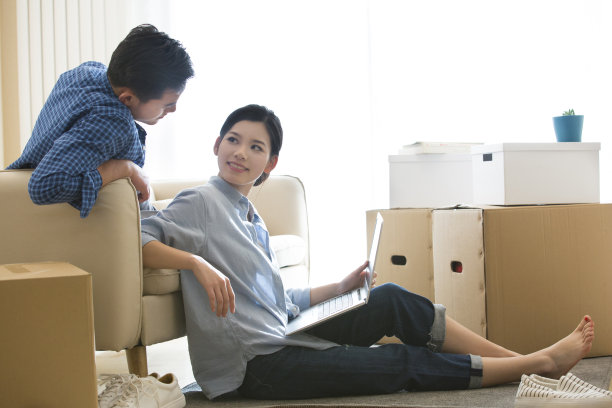 年轻夫妇搬进他们的新家，妻子坐在地板上使用笔记本电脑为新房子的室内设计-库存照片图片下载