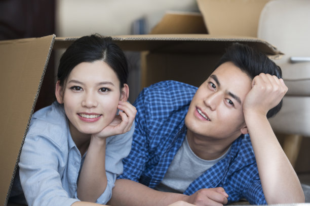 年轻夫妇搬进新家和装修房间，顽皮地躺下，进入一个纸板箱，正面的头像-库存照片图片下载