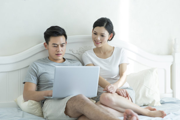 年轻夫妇在卧室的床上使用笔记本电脑在家装-库存照片图片下载