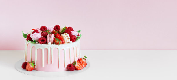 用马卡龙、覆盆子、草莓和糖玫瑰装饰的粉红蛋糕全景图。图片下载