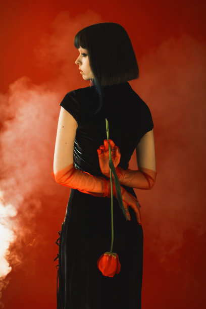 深色头发的亚洲妇女与郁金香在手与烟在工作室红色背景。时尚模特，白皙的皮肤，棕色的头发，黑色的衣服。手套的手。风格图片下载