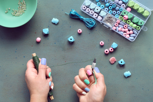 手工制作的首饰。盒子里有珠子，手里有工具。为自己制作手工珠宝或作为自制的定制礼物。平铺在灰色纹理背景上。图片下载