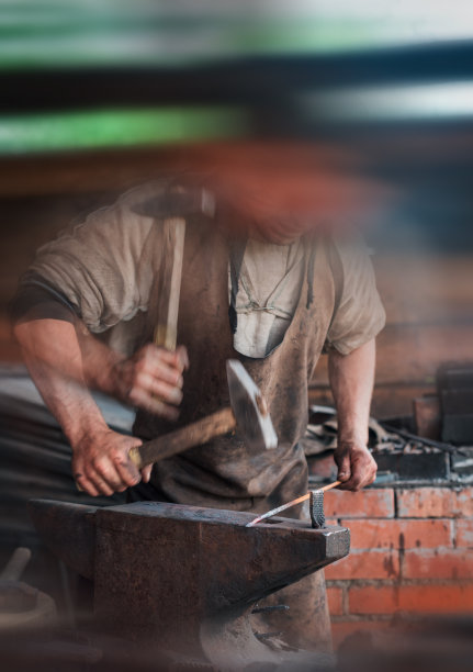 一个人的手与锤子的背景上一个正宗的复古锻炉与铁砧。图片下载