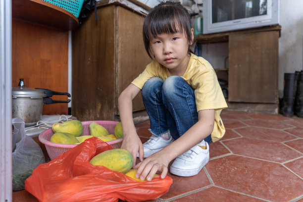 一个亚洲小女孩拿着一个木瓜放在厨房的地板上图片下载