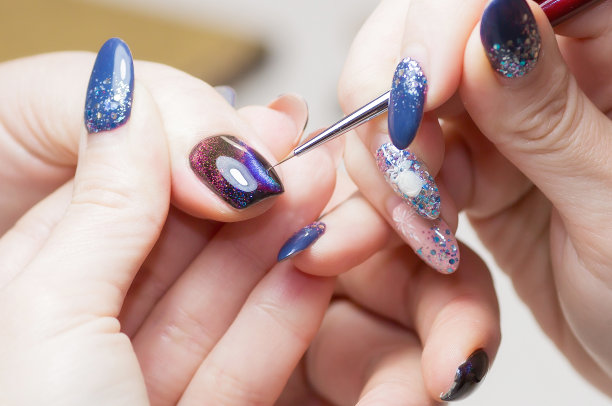 大师进行校正指甲油，深色指甲油与彩色污渍，特写照片。女人的手放在一个简单的背景上。图片下载