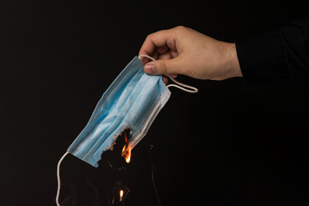 一个男人的手在黑暗的背景上拿着一个燃烧的一次性医用口罩图片下载
