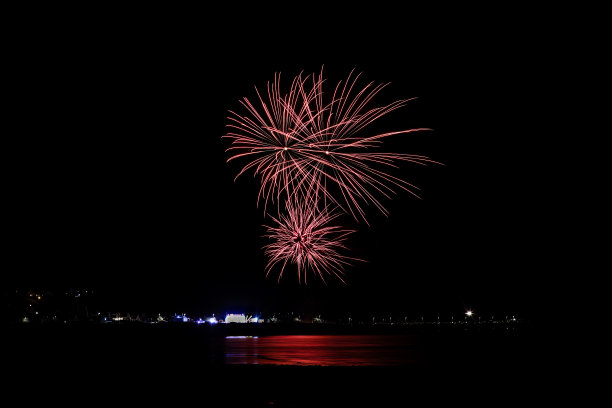 壮观的彩色烟花在壮丽的黑色天空下倒映在水面上的风景图片下载