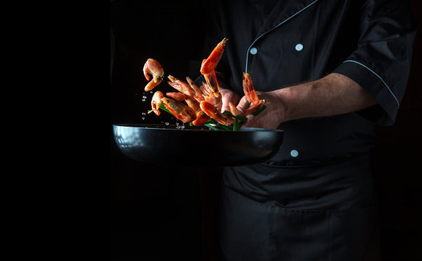 专业厨师在锅里和蔬菜一起煮虾。烹饪海鲜、健康素食和深色背景的食物。冻结。免费的广告空间图片下载