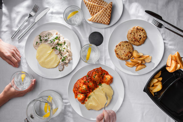 土豆泥配土豆、肉丸、炸土豆配肉排、加了酱汁的chapminions、加冰和柠檬的果汁、盛在玻璃杯里的橙汁，餐具放在铺着桌布和人手的桌子上图片下载