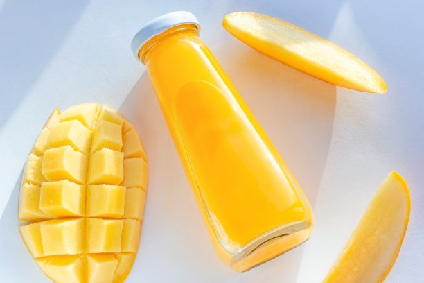 顶视图明黄色的芒果汁在一个玻璃瓶与切片新鲜芒果在白色背景上接近图片下载