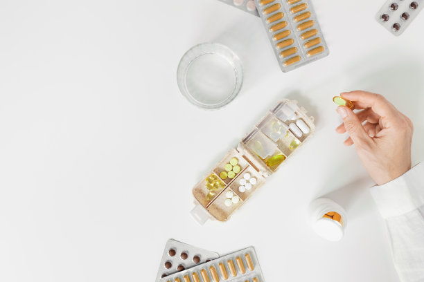 俯视图医疗片剂，胶囊，营养补充剂在妇女手中和一杯水在白色的桌子上。药盒，每周装维生素和矿物质的药盒。平躺图片下载