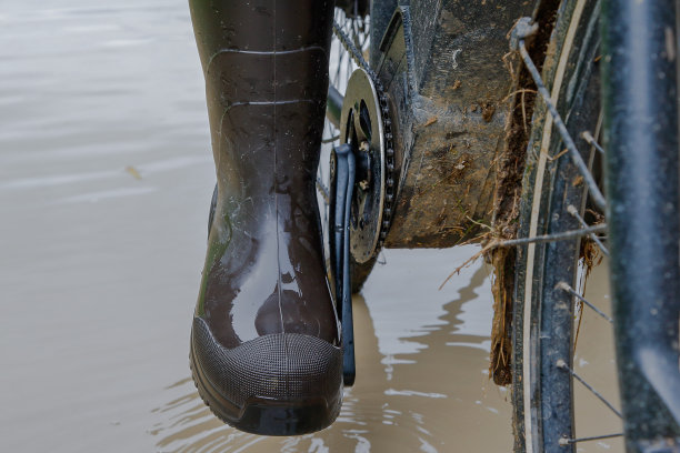 穿着胶靴骑着自行车走过雨季。图片下载