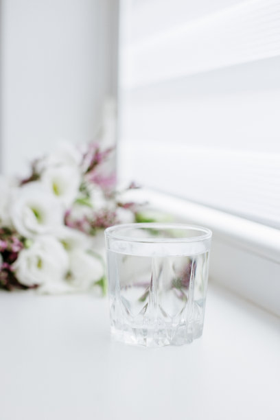 在花旁边的桌子上放一杯清水。关于饮品、健康生活方式和饮食的概念。图片下载