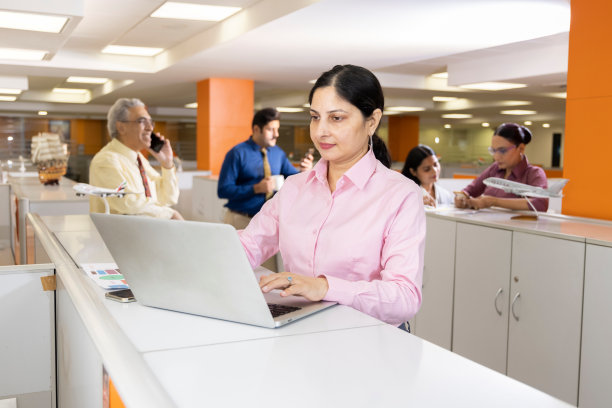 快乐的女商人在办公室使用笔记本电脑。图片下载