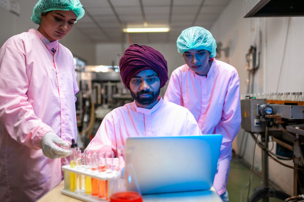 亚洲科学家在饮料厂的生产线上用试管检查果汁产品。制造商检查食品工业的质量。图片下载