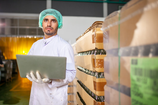 在饮料厂，工人拿着笔记本电脑在生产线上检查产品。制造商检查食品工业的质量。图片下载