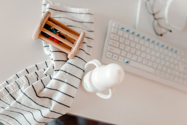 工作地点在家里。产假期间的工作地点。电脑桌，婴儿用品:奶瓶，拨浪鼓和毛巾。图片下载