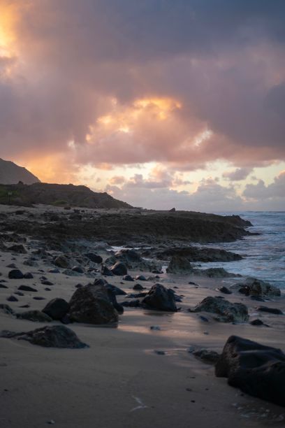 在夏威夷，日落时沙滩上的岩石向地平线延伸的垂直照片图片下载