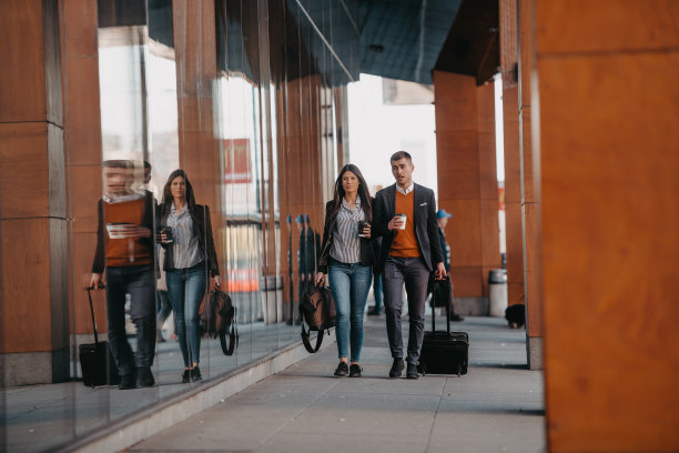 商务男女在出差时提着行李聊天，手里拿着新鲜的咖啡。经营理念图片下载