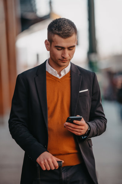 去机场候机楼。自信的商人旅行者走在城市的街道上，拉着他的行李箱，喝着咖啡，用智能手机说话图片下载