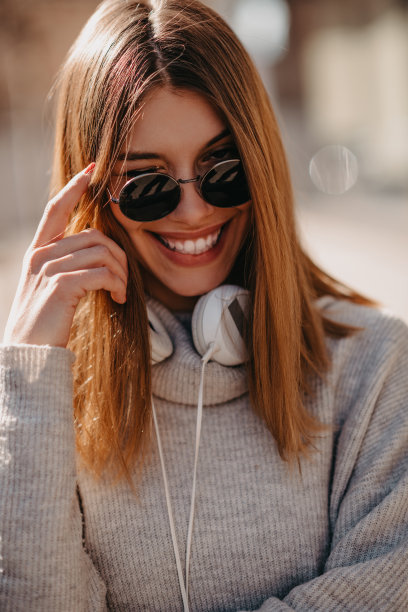 一个现代女孩戴着墨镜走在街上，戴着耳机听着音乐。图片下载