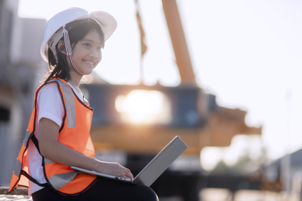 一个亚洲小女孩头戴安全帽，扮演建筑工程师和建筑师的角色，在建筑工地上使用笔记本电脑或平板电脑图片下载