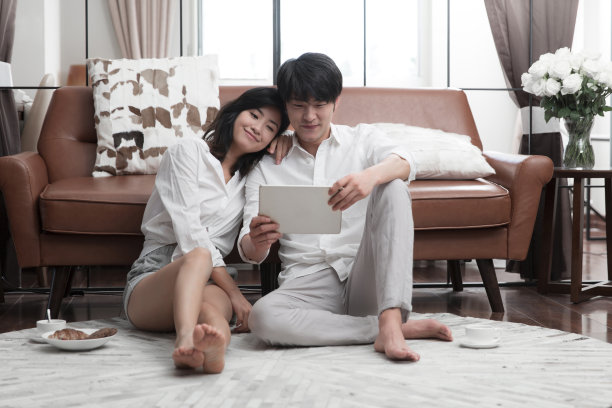 年轻的东亚夫妇坐在客厅地毯上使用平板电脑-库存照片图片下载