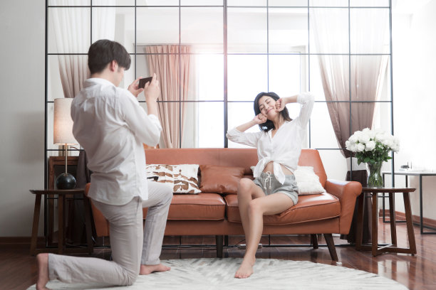 年轻的东亚夫妇在他们的客厅用智能手机拍照-库存照片图片下载