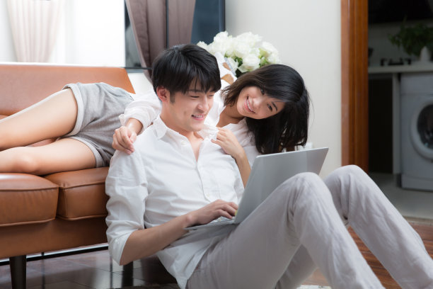 年轻的东亚夫妇坐在客厅地毯上使用笔记本电脑-库存照片图片下载