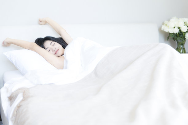 年轻的东亚妇女在现代家庭卧室的床上醒来-库存照片图片下载