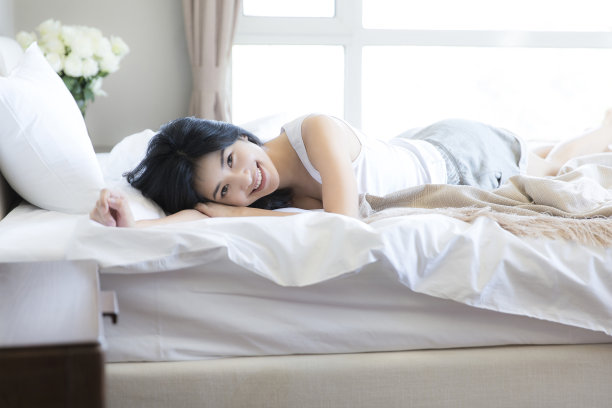 年轻的东亚妇女躺在她的背部在一个现代家庭卧室床-库存照片图片下载