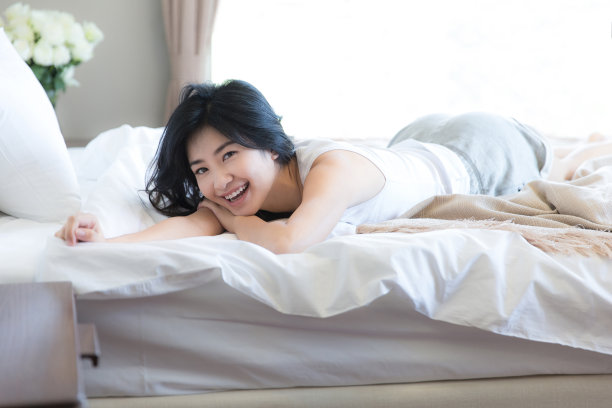 年轻的东亚妇女躺在她的背部在一个现代家庭卧室床-库存照片图片下载