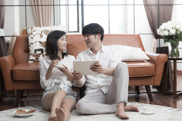 年轻的东亚夫妇坐在客厅地毯上使用平板电脑-库存照片图片下载