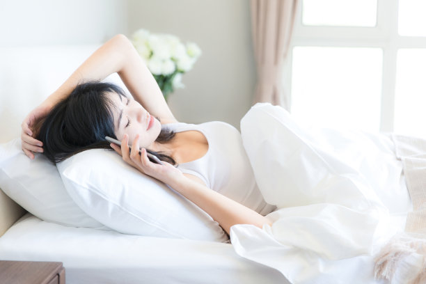 年轻的东亚妇女使用智能手机打电话躺在卧室床上的现代家庭-库存照片图片下载