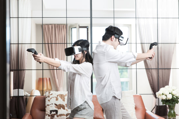 年轻的东亚夫妇在他们现代家庭的客厅里体验VR枪战游戏-库存照片图片下载