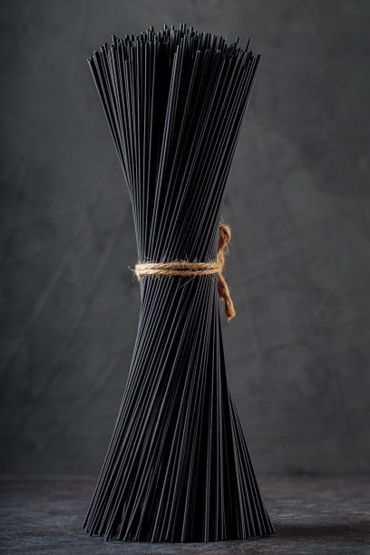 一束黑色意大利面，用麻绳绑在一起的意大利面。深色背景上的生黑意大利面。墨鱼墨干意大利面。特写镜头图片下载