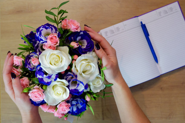 Flatlay。女性手里捧着一束五颜六色的玫瑰花。笔记本，日记和一支笔放在木桌上图片下载