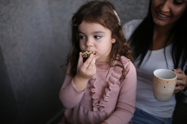 开心的小女孩在家里吃饼干逗妈妈笑。库存图片图片下载