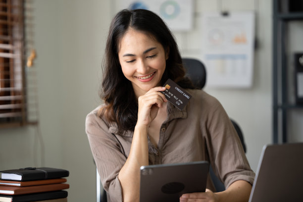 手拿塑料信用卡和使用笔记本电脑。网上购物的概念。在办公室电脑前工作的女商人图片下载