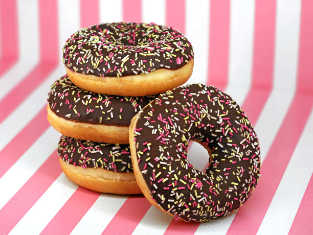 堆叠甜甜圈与巧克力糖霜和彩色撒在白色粉红色条纹背景，接近美味的甜甜圈图片下载