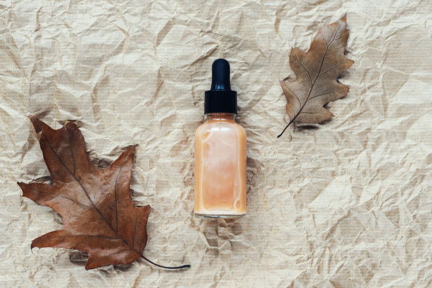 血清滴管瓶和棕色秋叶在米色皱褶纸背景。俯视图，平铺图片下载