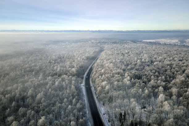 冬季景观鸟瞰图，积雪覆盖的树林和黑色沥青森林道路在寒冷的冬天图片下载