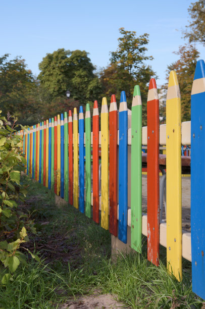 漂亮的栅栏是用木条做成的，漆得像彩色的大铅笔。城市公园里的儿童游乐场。背景是美丽的秋景图片下载