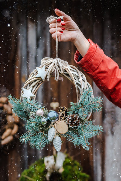 后视图年轻的女性潮人装饰家为圣诞节在门外。美丽的圣诞树花环在古老的木制乡村背景。图片下载