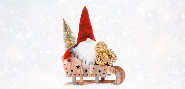 庆祝的背景。新年的概念。副本的空间。圣诞贺卡。圣诞小精灵戴着红帽子坐在木制雪橇上，旁边有一棵新年树和闪亮的球，站在雪地上，背景很亮。图片下载
