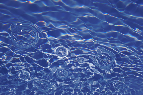 离焦模糊透明蓝色清澈平静的水面纹理与飞溅和气泡。新潮抽象的自然背景。阳光下的水波与复制空间。蓝色水彩闪亮的图片下载