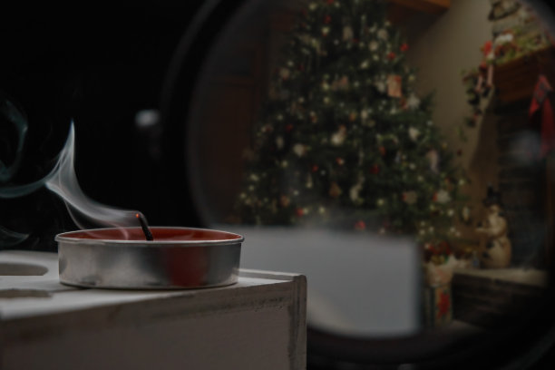 一根冒烟的蜡烛立在一个木箱上，背面黑色的背景上有镜子，反射出一棵圣诞树和玩具。有选择性的重点图片下载