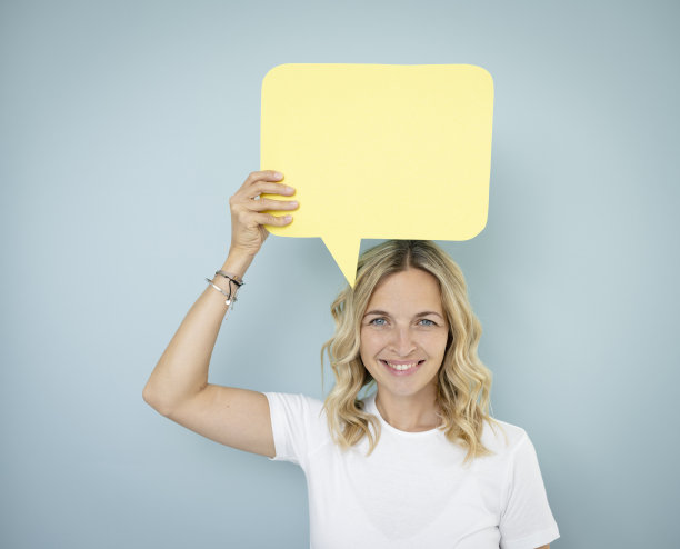 漂亮的金发卷发的年轻女子站在蓝色的墙前，拿着演讲泡沫图片下载