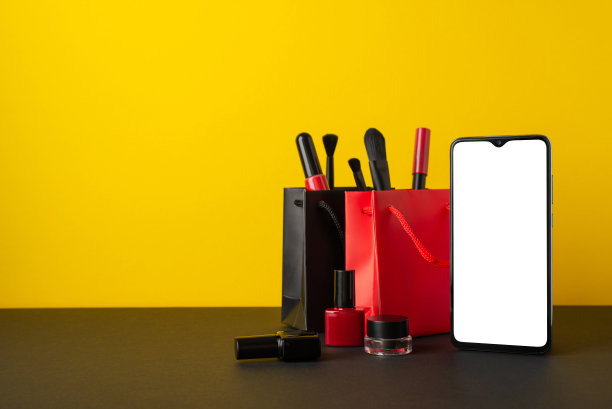 黑色星期五购物概念。照片的智能手机纸袋刷子，唇彩，眼线，眉毛凝胶和指甲油在桌面黄色的墙壁背景与copyspace图片下载