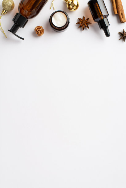 冬季护肤化妆品概念。顶视图垂直照片琥珀玻璃瓶奶油罐圣诞装饰金色小玩意儿肉桂棒和八角孤立的白色背景与空白图片下载